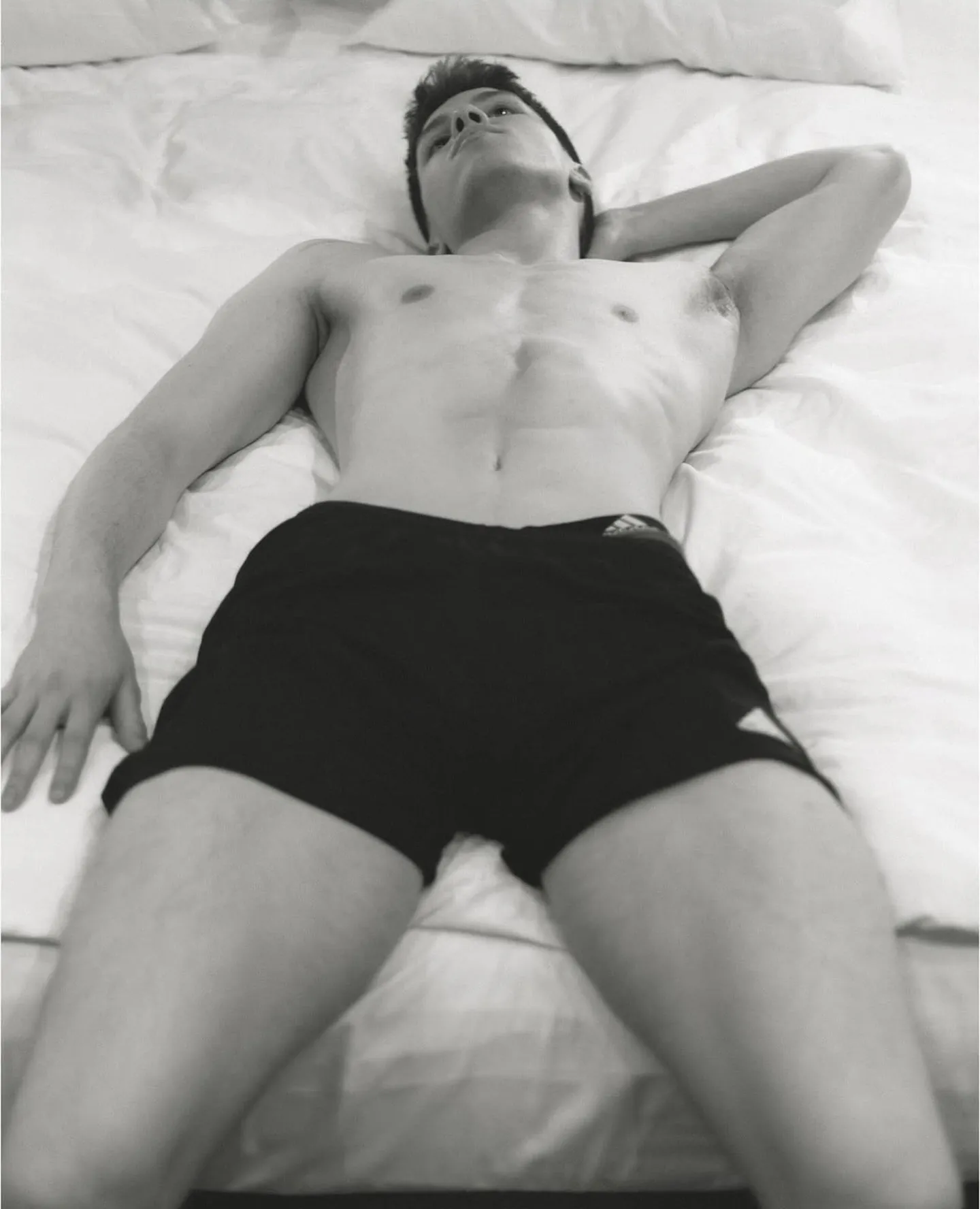 Black-and-white photo of a man in shorts relaxing on white sheets before a massage